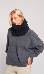 Femme portant un snood noir en alpaga doux et chaud, avec un pull gris et un pantalon beige.