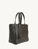 Profil du Petit sac cabas parisien pour femme en cuir de vachette tressé marron chocolat avec pompon assorti, modèle Ramita de LOXWOOD. Porté main avec anses de 16 cm.