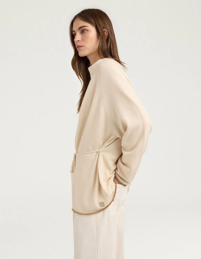 Profil du Cardigan à col rond pour femme en pure laine crème, modèle Klak Bis de la marque MOMONI. Présente des manches raglan amples, une fermeture à ruban de laine à nouer et des liserés en lurex doré.