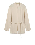 Cardigan à col rond pour femme en pure laine crème, modèle Klak Bis de la marque MOMONI. Présente des manches raglan amples, une fermeture à ruban de laine à nouer et des liserés en lurex doré.