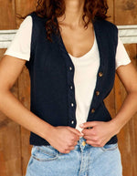 Silhouette avec le Gilet sans manches pour femme en maille bleu marine à col V et boutons en corne, modèle Melba de La Petite Étoile. Présente des finitions torsadées au col, aux emmanchures et au bas.