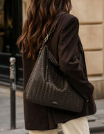 Silhouette avec le Sac hobo pour femme en cuir de vachette tressé marron chocolat avec pompon assorti, modèle Sharon de LOXWOOD. Porté épaule avec fermeture zippée.