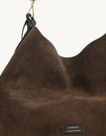 Vue de face du Sac hobo pour femme en cuir velours marron chocolat avec pompon assorti et porté épaule, modèle Sharon de la marque Loxwood.