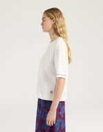 Profil du T-shirt oversize à manches courtes pour femme en jersey de coton blanc lurex, modèle Iora de la marque MOMONI. Présente une encolure ronde et de petites fentes latérales.