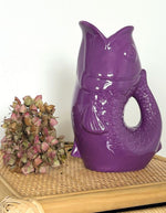 Ambiance déco avec le Vase pichet poisson en faïence violette brillante, marque Opjet. Silhouette sculpturale rétro des années 60, hauteur de 25,3 cm, utilisable comme carafe ou vase.