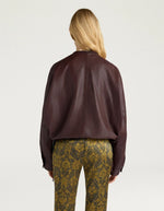 Dos de la Veste bomber courte pour femme en cuir d'agneau marron, modèle Kaldor de la marque MOMONI. Présente une coupe carrée avec cordon de serrage au bas et des boutons-pression en laiton vieilli.