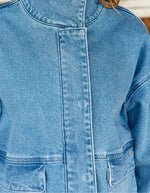 Vue de face de la Veste courte en jean bleu stone pour femme avec col montant et broderie en relief dans le dos, modèle Velmo de La Petite Étoile. Présente des poches à rabat et une coupe droite.