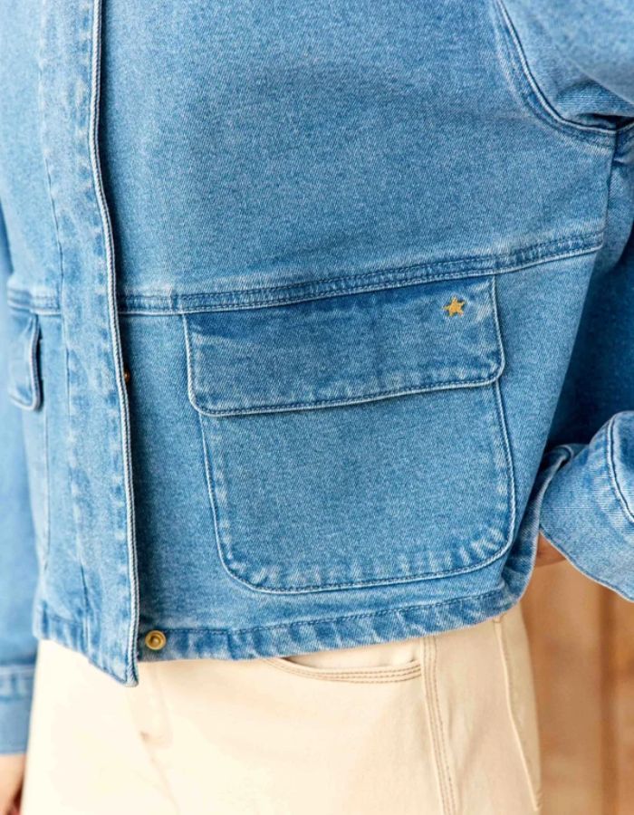 Poche de la Veste courte en jean bleu stone pour femme avec col montant et broderie en relief dans le dos, modèle Velmo de La Petite Étoile. Présente des poches à rabat et une coupe droite.