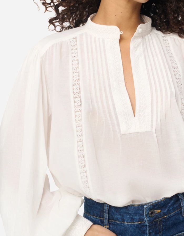 Blouse blanche Gania en voile de coton avec col officier, encolure fendue et empiècements plissés.