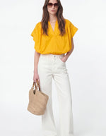 Blouse Cory Safran Vanessa Bruno en voile de coton, col V, manches kimono, portée avec un jean blanc et un sac en paille.