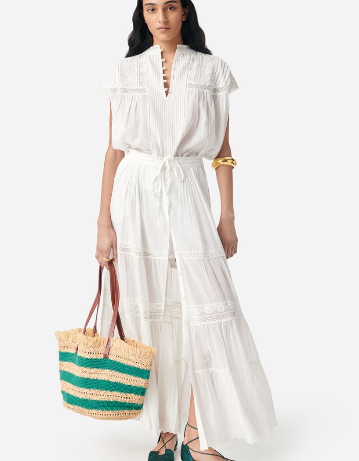Blouse Ganu Blanche fluide et légère avec dentelle, manches volantées, portée avec jupe longue et sac en paille.