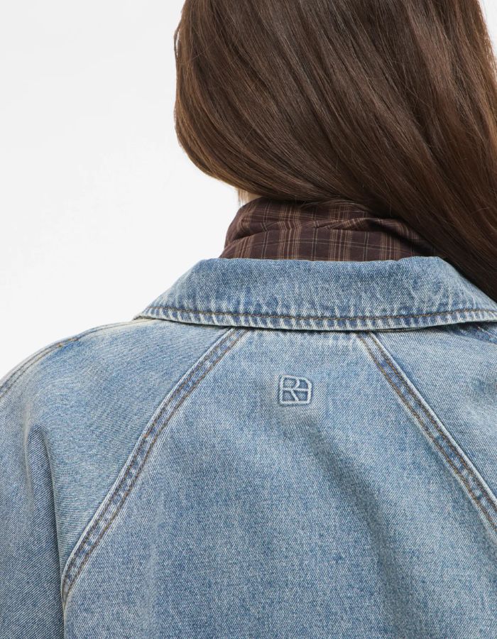 Dos du col du Blouson style bomber en jean pour femme de couleur bleu clair délavé Light Blue Denim, modèle Tiana de la marque Rouge Edit. Présente un col chemise évasé, une fermeture à glissière cachée sous des boutons-pression dorés mats Dull Gold et des brides de serrage ajustables.