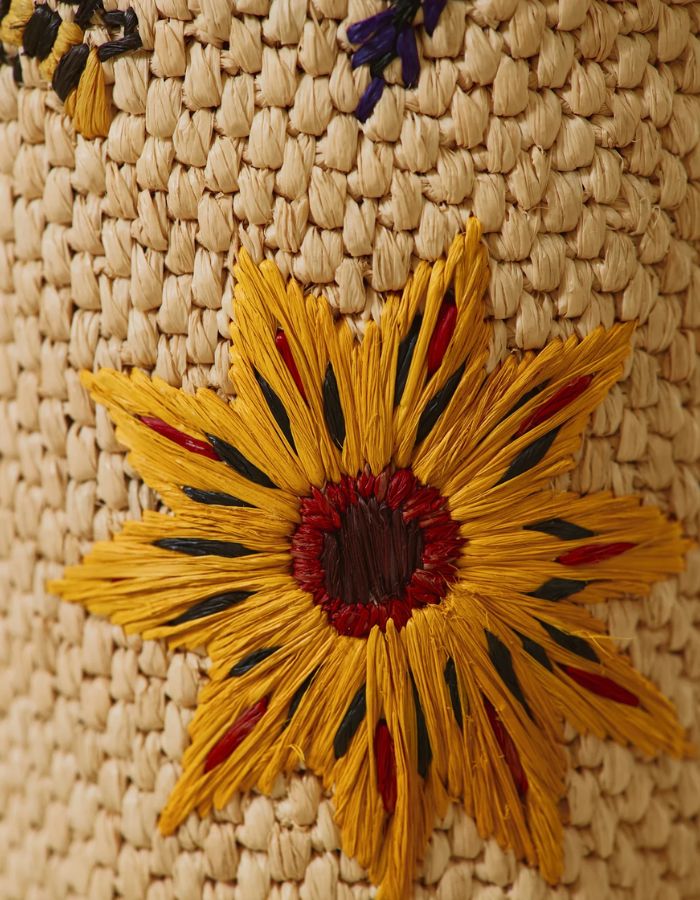 Détail de la Bougie parfumée de luxe Vony Ahitra par Baobab Collection. Photophore recouvert de raphia naturel avec broderies artisanales colorées représentant des fleurs des champs (coquelicots, lavande). Design textile fait main à Madagascar.