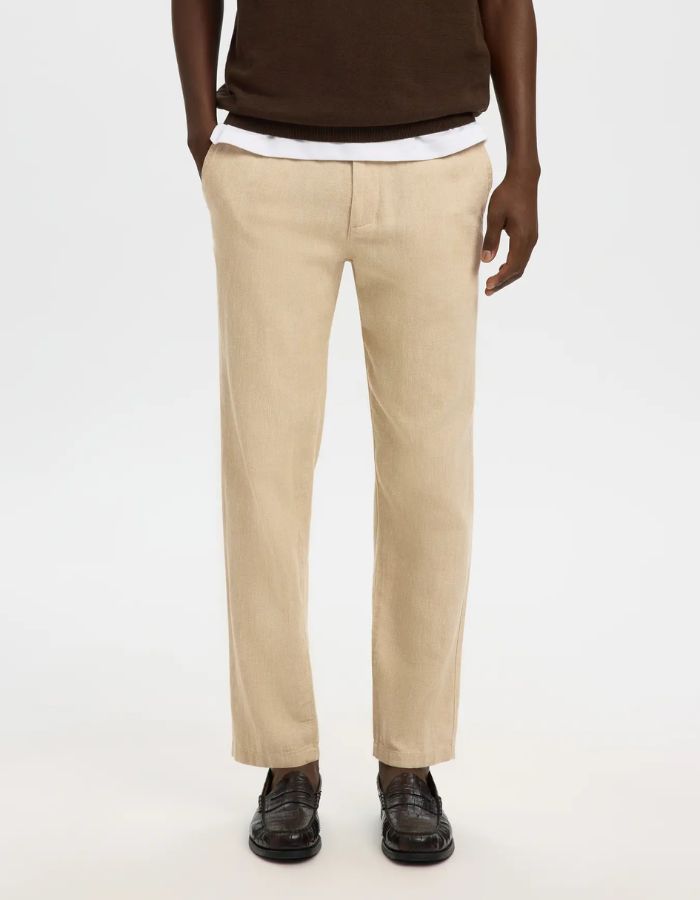 Pantalon Brody Slim Tapered en lin et coton beige, porté avec un t-shirt blanc et un pull marron.