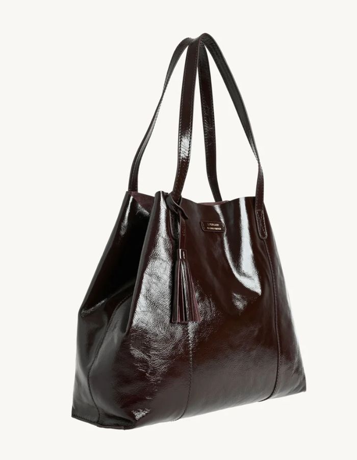 Profil du Grand sac cabas souple pour femme en cuir de vachette vernis bordeaux, modèle Odéon de la marque LOXWOOD. Présente deux anses de porté épaule, une patte de fermeture magnétique et un pompon amovible en cuir.