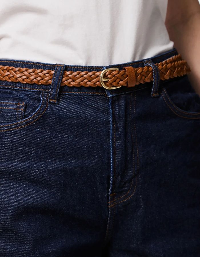 Gros plan sur la Ceinture fine pour femme modèle Avery de la marque Pieces, en cuir véritable tressé de couleur marron cognac avec une boucle métallique arrondie