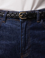 Gros plan sur la Ceinture fine pour femme modèle Avery de la marque Pieces, en cuir véritable tressé de couleur noire avec une boucle métallique arrondie classique.