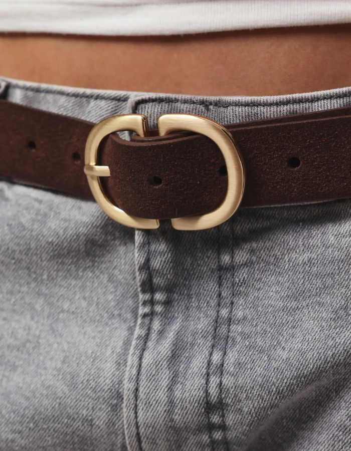 Boucle de la Ceinture pour femme en cuir suédé véritable de couleur marron chocolat Hot Fudge, modèle Juva de la marque Pieces. Présente une bande de 3 cm de large en daim mat et doux, fermée par une boucle rectangulaire en métal doré brossé mat.