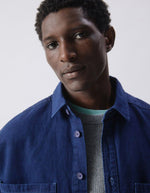 Détail du haut de la Chemise en denim brut bleu foncé pour homme, modèle Comow de la marque American Vintage. Coupe ample et oversize, dotée de manches longues, de deux poches plaquées sur la poitrine et d'un col chemise classique. Au dos, le logo de la marque apparaît discrètement grâce à une finition gravée au laser