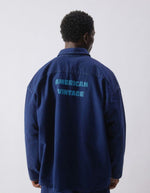 Silhouette de dos avec la Chemise en denim brut bleu foncé pour homme, modèle Comow de la marque American Vintage. Coupe ample et oversize, dotée de manches longues, de deux poches plaquées sur la poitrine et d'un col chemise classique. Au dos, le logo de la marque apparaît discrètement grâce à une finition gravée au laser