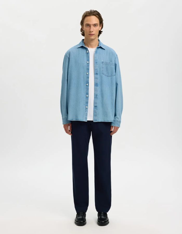 Homme portant une chemise en jean bleu clair Carlo, coupe regular, avec poche poitrine et boutons blancs.