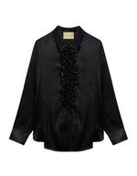Chemisier long fluide noir pour femme au fini métallisé laminé brillant, modèle Bilancia Bis de la marque Momoni. Présente une coupe oversize avec de grands volants drapés, un col bateau asymétrique tombant sur l'épaule et des manches longues terminées par de hauts poignets à boutons recouverts.