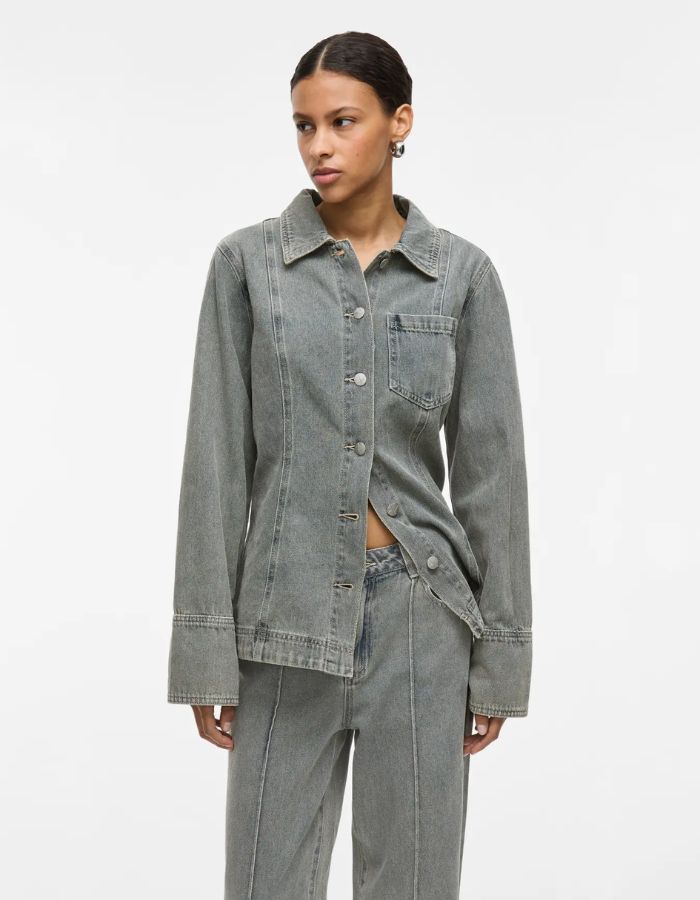 Mannequin portant une chemise en denim gris clair avec col, manches longues, fermeture boutonnée et poche poitrine.
