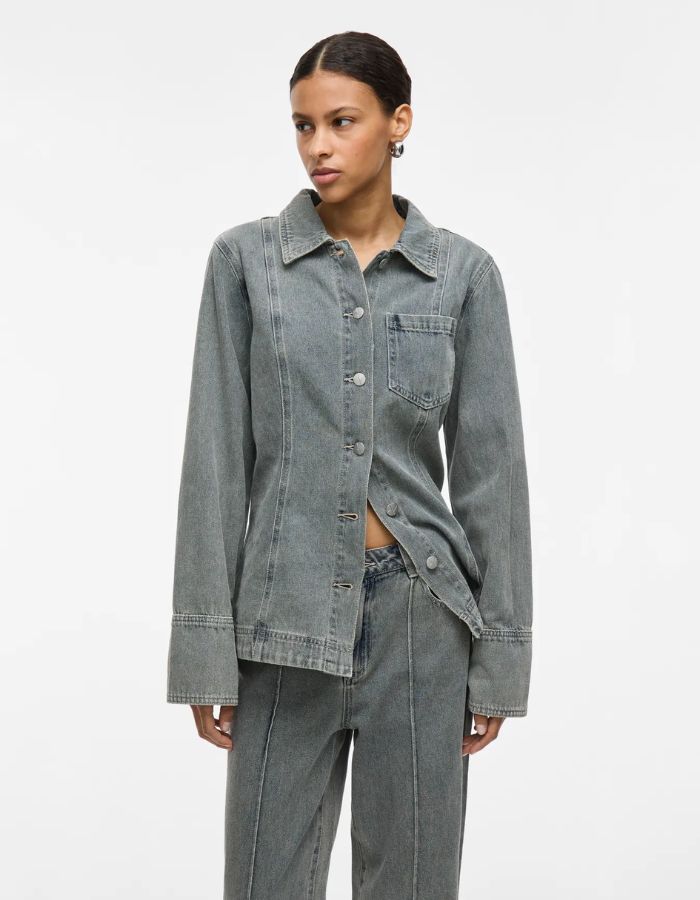 Femme portant une chemise en denim bleu clair Vivian avec col, boutons et poche poitrine.