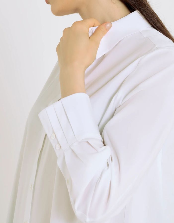 Manche de la Chemise évasée pour femme en popeline de coton stretch blanc optique, modèle Dorothea de la marque Hana San. Présente une coupe patineuse, une découpe au dos et des poignets plissés avec boutons en nacre.