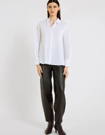 Silhouette avec la Chemise évasée pour femme en popeline de coton stretch blanc optique, modèle Dorothea de la marque Hana San. Présente une coupe patineuse, une découpe au dos et des poignets plissés avec boutons en nacre.