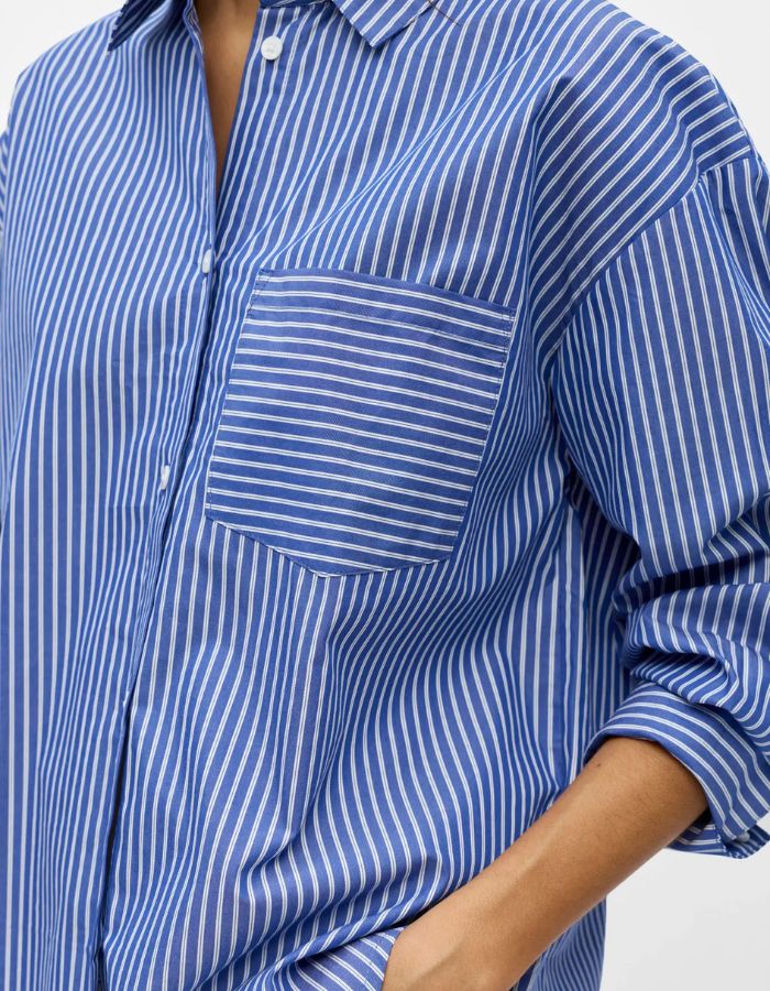 Détail de la Chemise à manches longues pour femme modèle Zila de la marque Object. Tissu tissé fluide à rayures verticales bleu Clématite et blanc, dotée d'un col classique, d'une fermeture boutonnée et d'une poche plaquée sur la poitrine.