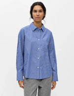 Vue de face de la Chemise à manches longues pour femme modèle Zila de la marque Object. Tissu tissé fluide à rayures verticales bleu Clématite et blanc, dotée d'un col classique, d'une fermeture boutonnée et d'une poche plaquée sur la poitrine.