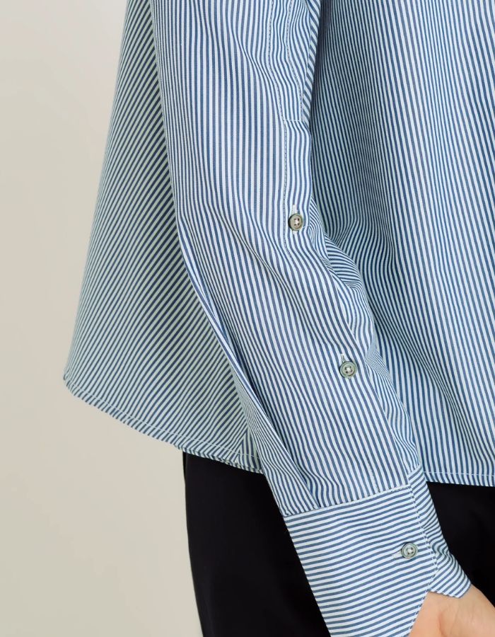 Manche de la Chemise évasée à rayures bleu indigo pour femme, modèle Grace de la marque Hana San. Présente une patte de boutonnage cachée, une emmanchure marteau et de longues pattes poignets boutonnées.
