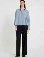 Silhouette avec la Chemise évasée à rayures bleu indigo pour femme, modèle Grace de la marque Hana San. Présente une patte de boutonnage cachée, une emmanchure marteau et de longues pattes poignets boutonnées.