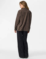 Silhouette de dos avec la Chemise ample pour femme en velours côtelé à manches longues, modèle Effi de la marque Pieces. Tissu corduroy de couleur marron foncé chocolat Hot Fudge, avec des poches de poitrine boutonnées et des poignets élastiqués.