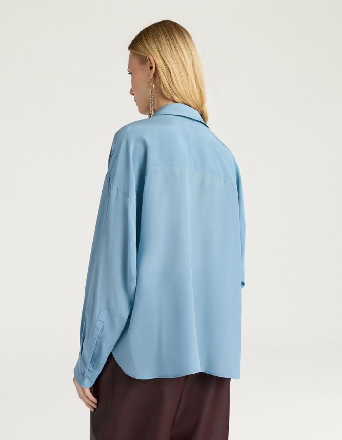 Dos du Chemisier oversize en pure soie de couleur bleu céruléen uni, modèle Pitanga de la marque Momoni. Présente une coupe ample et fluide avec un col bateau, une fermeture boutonnée originale sur le haut des épaules et des manches longues à poignets à la française.