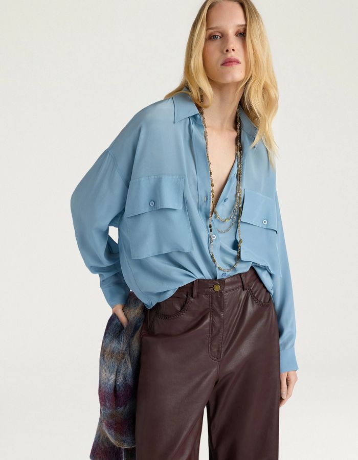 Vue de face du Chemisier oversize en pure soie de couleur bleu céruléen uni, modèle Pitanga de la marque Momoni. Présente une coupe ample et fluide avec un col bateau, une fermeture boutonnée originale sur le haut des épaules et des manches longues à poignets à la française.