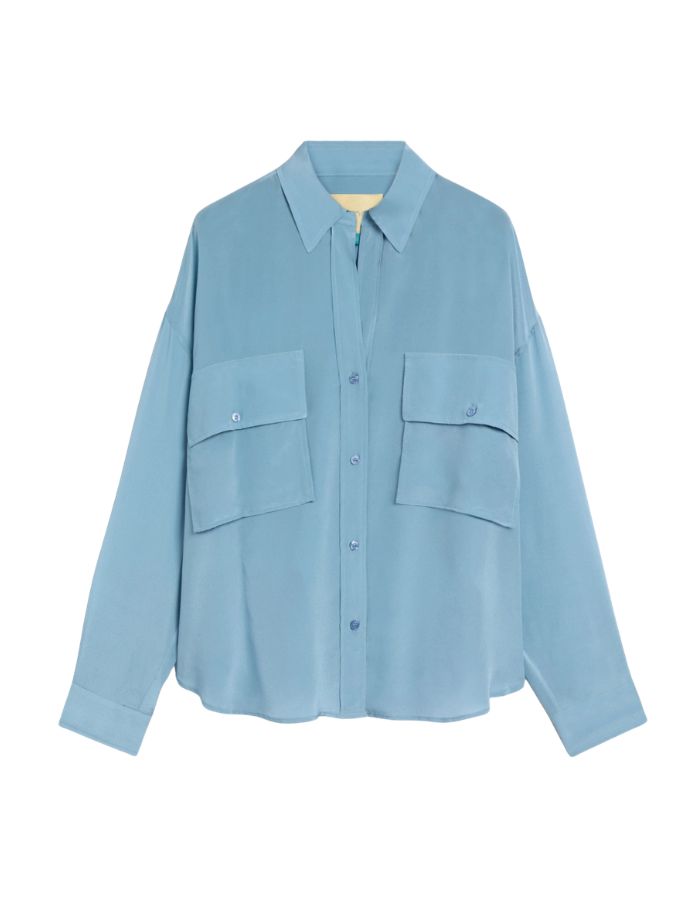 Chemisier oversize en pure soie de couleur bleu céruléen uni, modèle Pitanga de la marque Momoni. Présente une coupe ample et fluide avec un col bateau, une fermeture boutonnée originale sur le haut des épaules et des manches longues à poignets à la française.