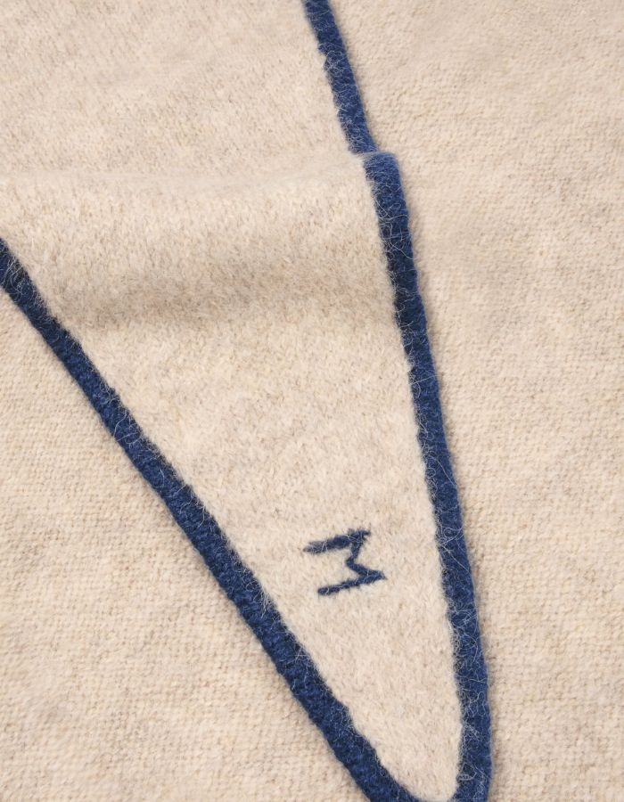 Détail du logo sur l'Écharpe triangle pour femme en baby alpaga doux avec liseré contrastant bleu marine chic, modèle Écharpe Elly N°218 Cord Comedia de la marque MOISMONT.