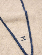 Détail du logo sur l'Écharpe triangle pour femme en baby alpaga doux avec liseré contrastant bleu marine chic, modèle Écharpe Elly N°218 Cord Comedia de la marque MOISMONT.