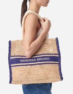 Grand panier en raphia tressé beige avec motif ajouré, bandes et logo Vanessa Bruno brodé bleu marine.