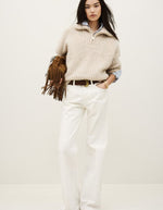 Mannequin portant un jean flare Badou écru taille basse en coton biologique, avec un pull beige et un sac à franges marron.