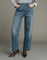 Vue de face du Jean droit pour femme en denim bleu délavé avec plis marqués devant et dos, modèle Jerry de la marque SOEUR. Présente une coupe droite 5 poches, une fermeture boutonnée zippée et un patch en cuir au dos.