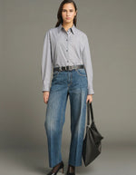 Silhouette avec le Jean droit pour femme en denim bleu délavé avec plis marqués devant et dos, modèle Jerry de la marque SOEUR. Présente une coupe droite 5 poches, une fermeture boutonnée zippée et un patch en cuir au dos.