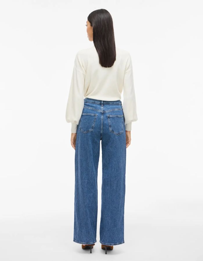 Silhouette de dos avec le Jean large pour femme de couleur bleu moyen Medium Blue Denim, modèle Reya de la marque Vila. Présente une taille haute ajustée et des jambes amples fluides (coupe Frida), avec une fermeture par zip.