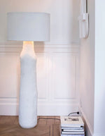 Lampadaire Earth Marie Michielssen en papier mâché blanc, avec base texturée et abat-jour cylindrique.