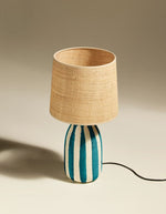 Lampe Palmaria Maison Sarah Lavoine avec pied en céramique rayé bleu et blanc, abat-jour en rabane.
