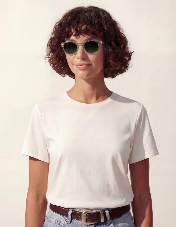 Femme avec les Lunettes de soleil unisexes IZIPIZI modèle #C de forme carrée vintage épaisse. La monture brillante est d'un coloris vert doux et légèrement translucide nommé Green Fields, associée à des verres solaires polarisés protecteurs