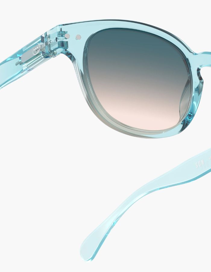 Gros plan sur les Lunettes de soleil unisexes IZIPIZI modèle #C de forme carrée vintage épaisse. La monture brillante est d'une couleur bleu turquoise translucide inspirée de la pierre turquoise, associée à des verres solaires bleus.