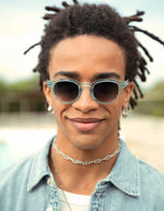 Homme avec les Lunettes de soleil unisexes IZIPIZI modèle #C de forme carrée vintage épaisse. La monture brillante est d'une couleur bleu turquoise translucide inspirée de la pierre turquoise, associée à des verres solaires bleus.